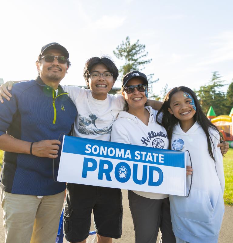 Family of four with two parents and two kids holding a Sonoma State Proud banner